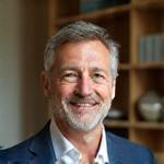 Portrait of Michael B., smiling in his modern London living room with a bespoke bookshelf behind him.
